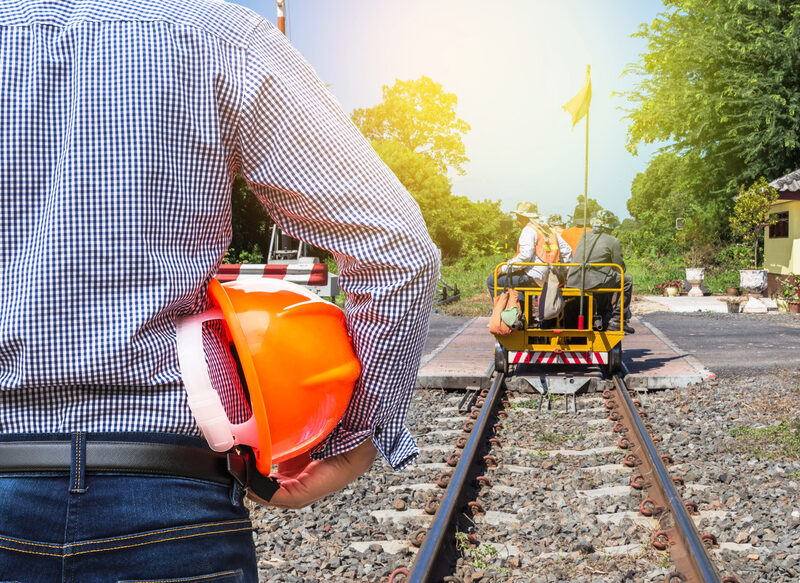 engineer holding yellow safety helmet with workers on motor cart for inspection maintenance of railway background